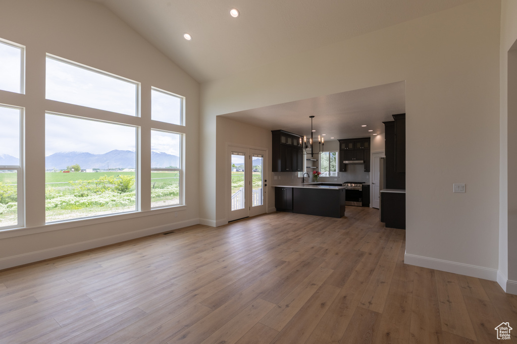 Unfurnished living room with a chandelier, light wood finished floors, a sink, baseboards, and recessed lighting
