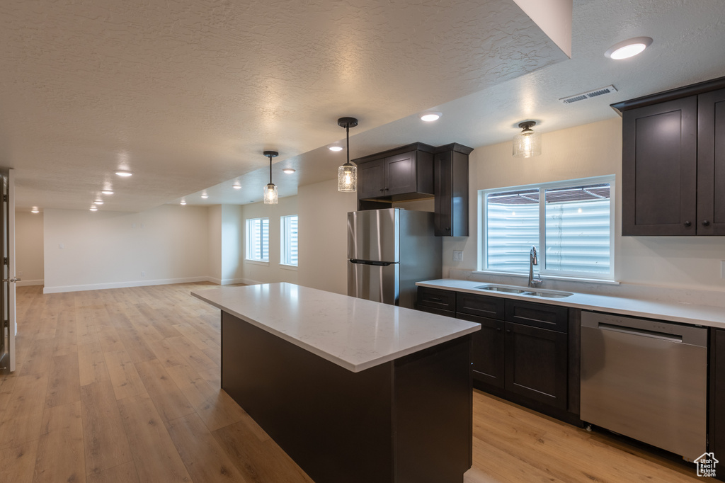 Kitchen with appliances with stainless steel finishes, a sink, a textured ceiling, light countertops, and a center island