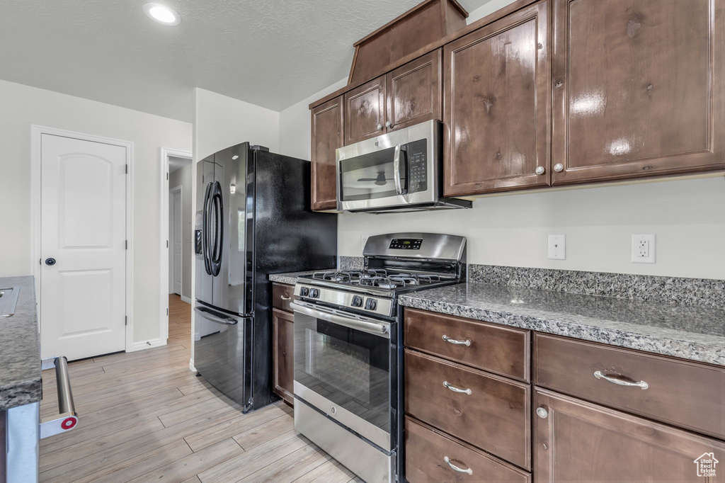 Kitchen with light wood-type flooring, appliances with stainless steel finishes, and dark brown cabinets