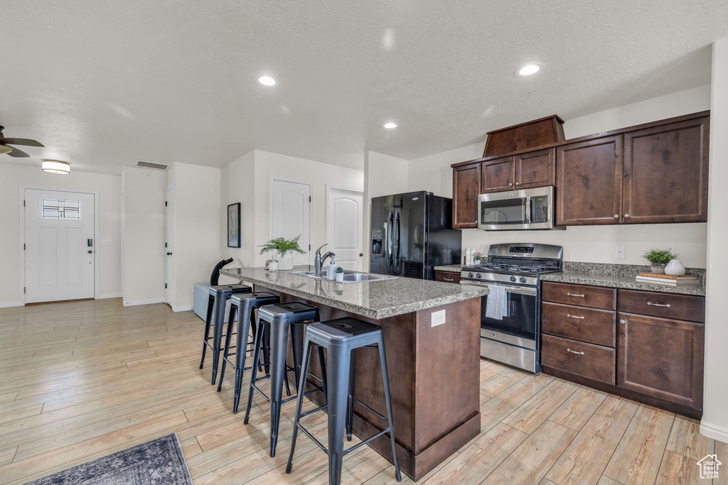 Kitchen featuring an island with sink, light hardwood / wood-style floors, sink, stainless steel appliances, and a kitchen bar