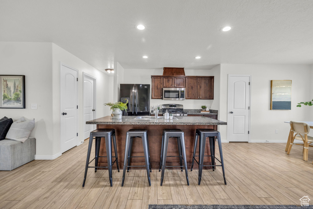 Kitchen featuring light hardwood / wood-style flooring, a kitchen island with sink, appliances with stainless steel finishes, and a breakfast bar