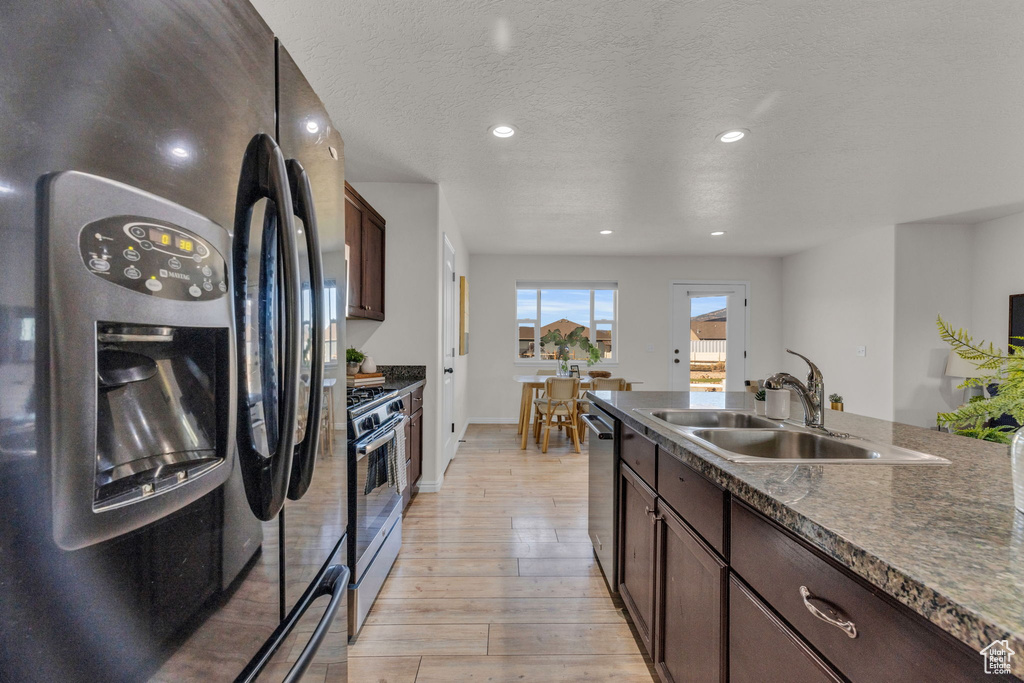 Kitchen with a textured ceiling, light hardwood / wood-style floors, sink, appliances with stainless steel finishes, and dark brown cabinetry