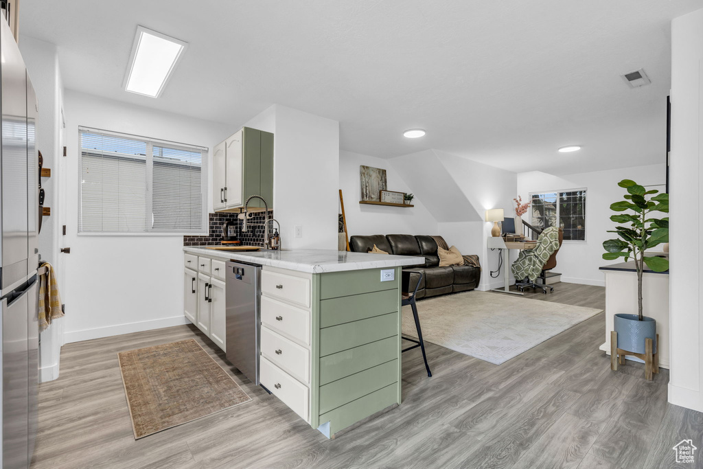 Kitchen with stainless steel appliances, decorative backsplash, sink, light wood-type flooring, and kitchen peninsula