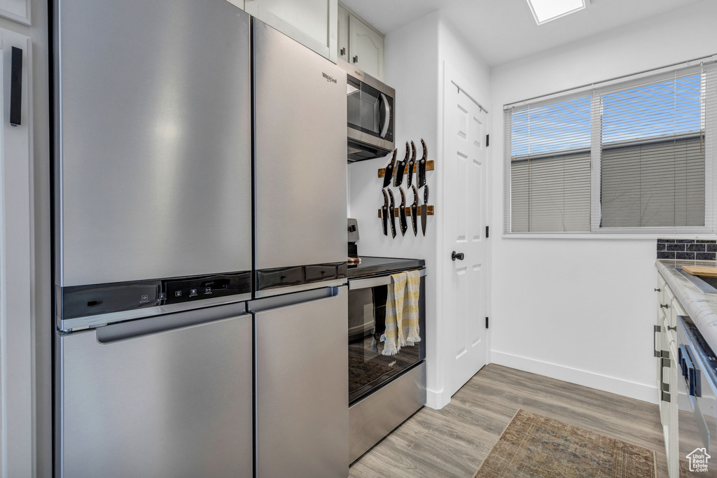 Kitchen featuring stainless steel appliances, light hardwood / wood-style floors, and white cabinets