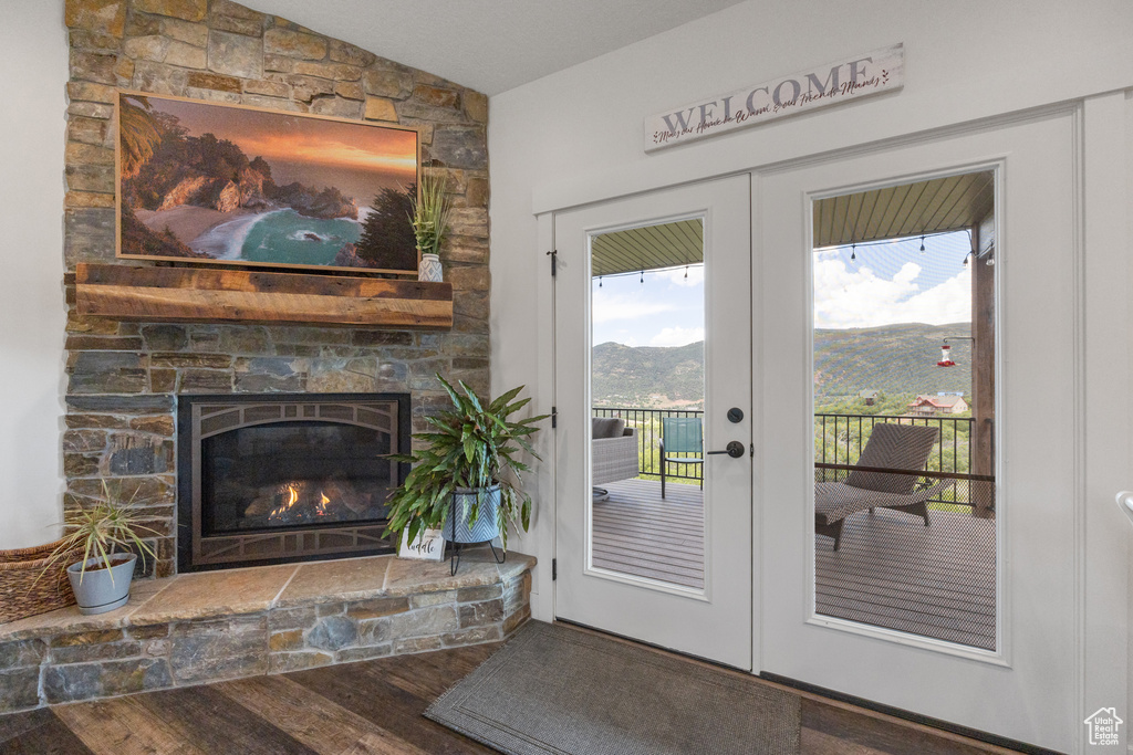 Doorway to outside with vaulted ceiling, hardwood / wood-style flooring, a stone fireplace, and french doors