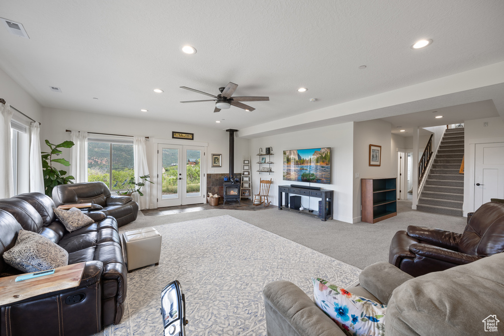 Carpeted living room with ceiling fan, french doors, and a wood stove