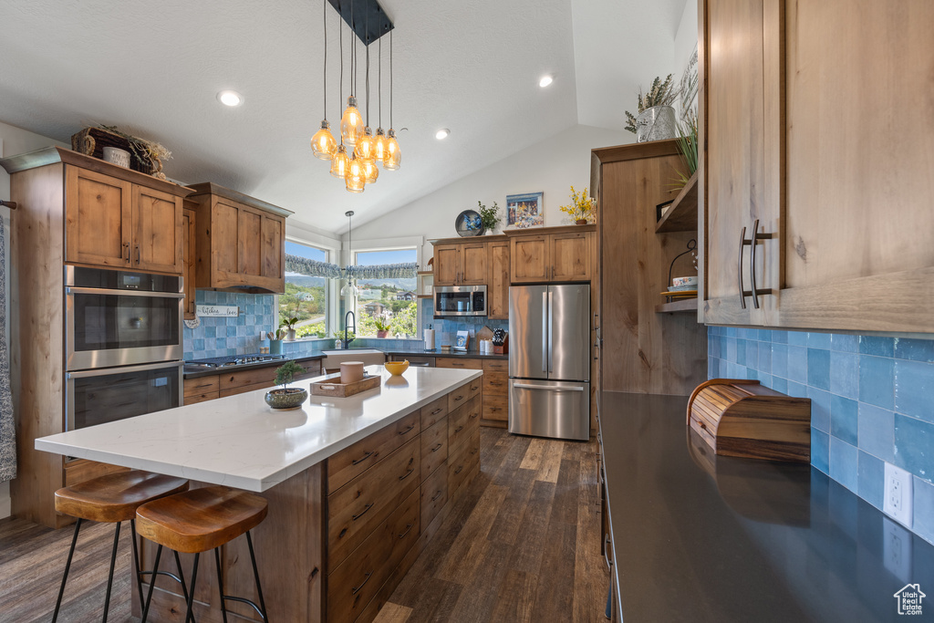 Kitchen featuring stainless steel appliances, dark hardwood / wood-style floors, tasteful backsplash, a kitchen island, and vaulted ceiling