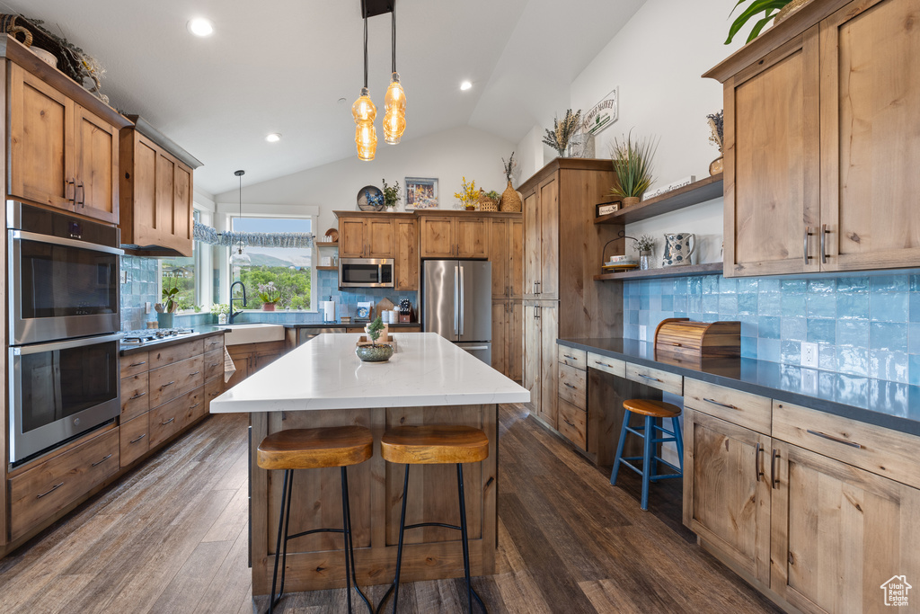 Kitchen featuring backsplash, dark hardwood / wood-style floors, pendant lighting, vaulted ceiling, and stainless steel appliances