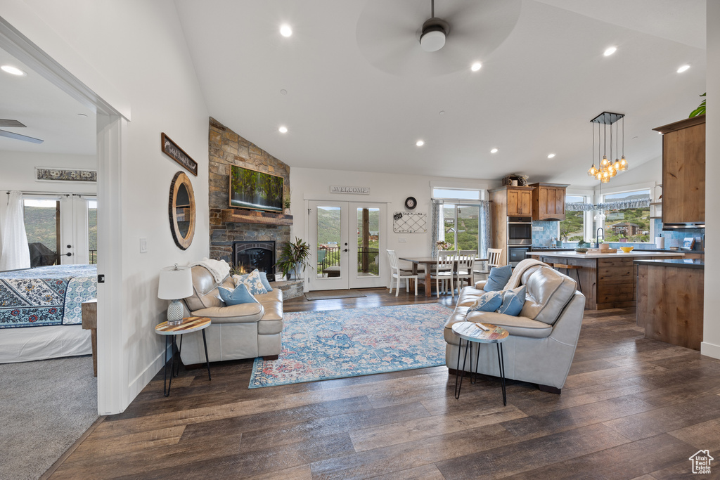 Living room featuring a stone fireplace, french doors, dark carpet, ceiling fan, and lofted ceiling