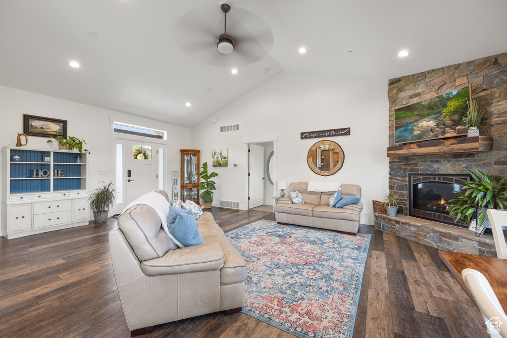 Living room featuring ceiling fan, high vaulted ceiling, dark wood-type flooring, and a stone fireplace