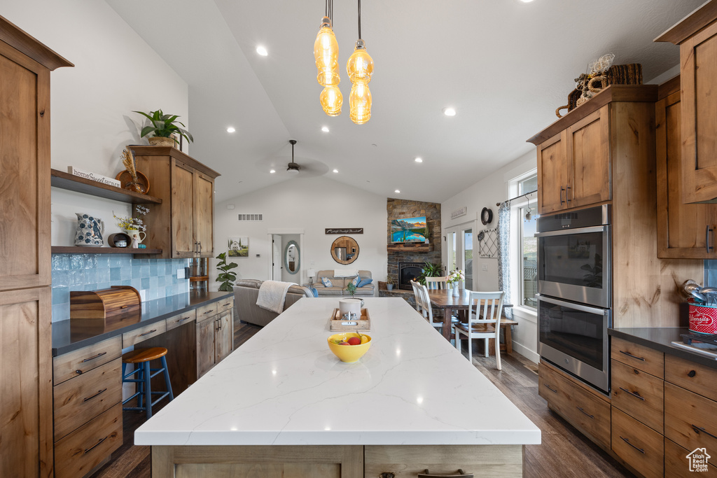 Kitchen featuring tasteful backsplash, stainless steel double oven, a fireplace, lofted ceiling, and dark wood-type flooring