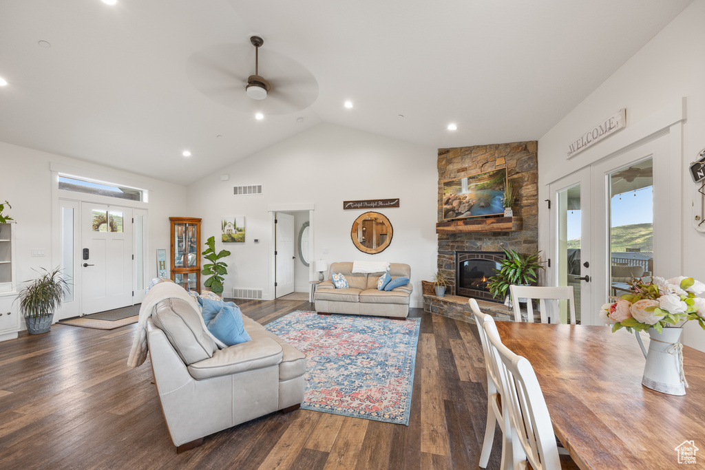 Living room with ceiling fan, dark hardwood / wood-style floors, high vaulted ceiling, and a stone fireplace