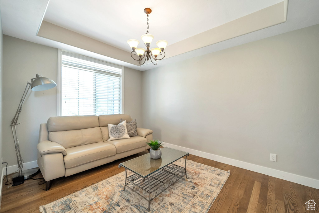 Living room with a chandelier, wood-type flooring, and a tray ceiling