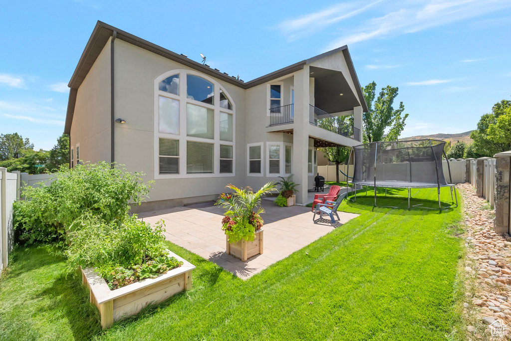 Rear view of property featuring a patio area, a yard, a trampoline, and a balcony