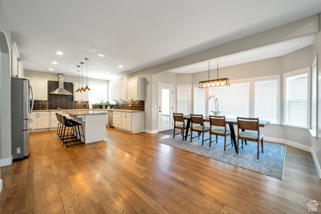 Kitchen with light wood-type flooring, appliances with stainless steel finishes, a kitchen island, and wall chimney range hood