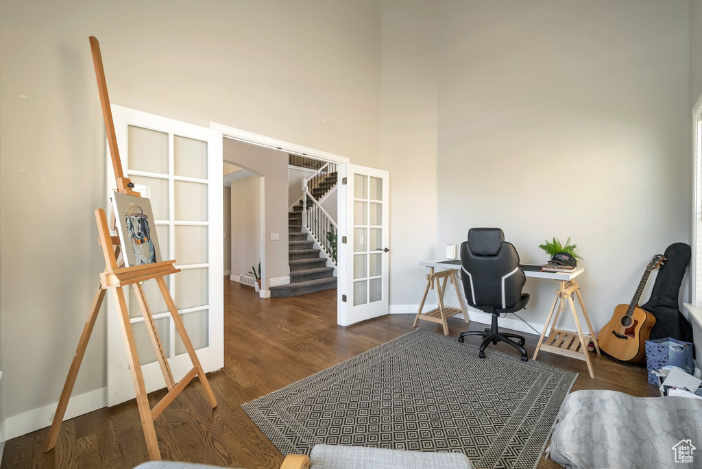 Office area with dark hardwood / wood-style flooring, a towering ceiling, and french doors