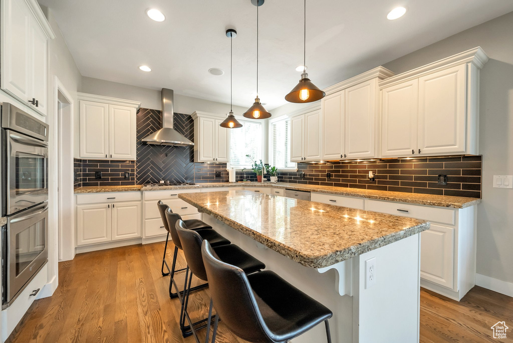 Kitchen with backsplash, wall chimney range hood, a kitchen island, and light wood-type flooring