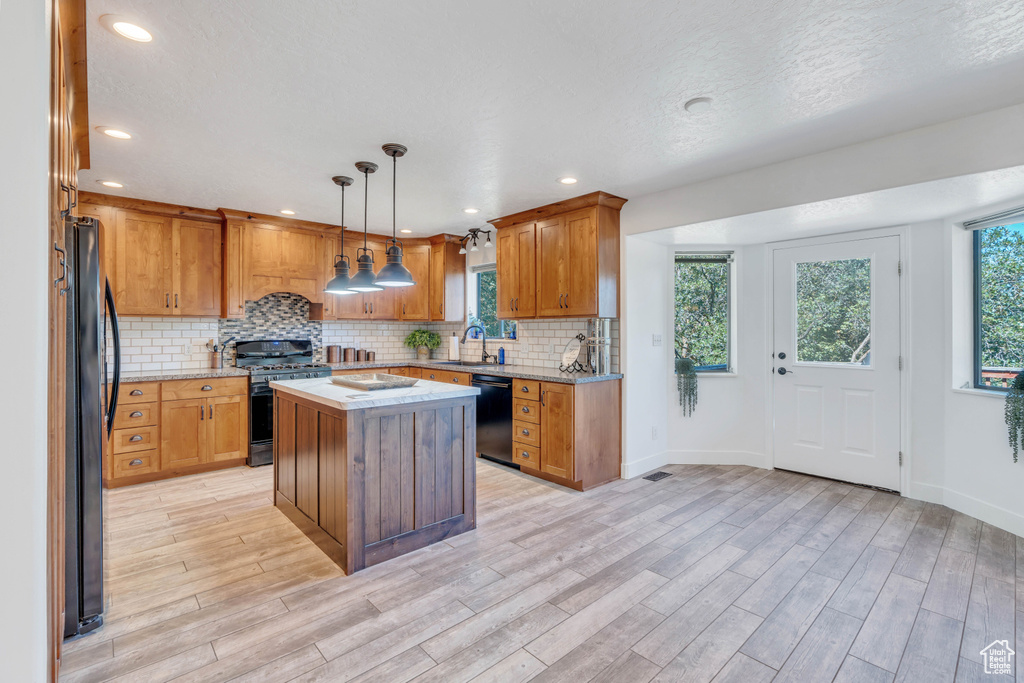 Kitchen with light hardwood / wood-style flooring, tasteful backsplash, decorative light fixtures, black appliances, and a center island