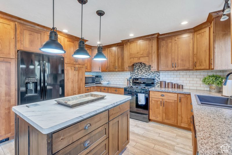 Kitchen featuring black fridge, light hardwood / wood-style floors, gas stove, tasteful backsplash, and hanging light fixtures