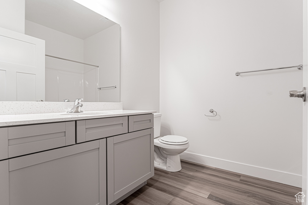 Full bath with vanity, toilet, wood finished floors, and baseboards