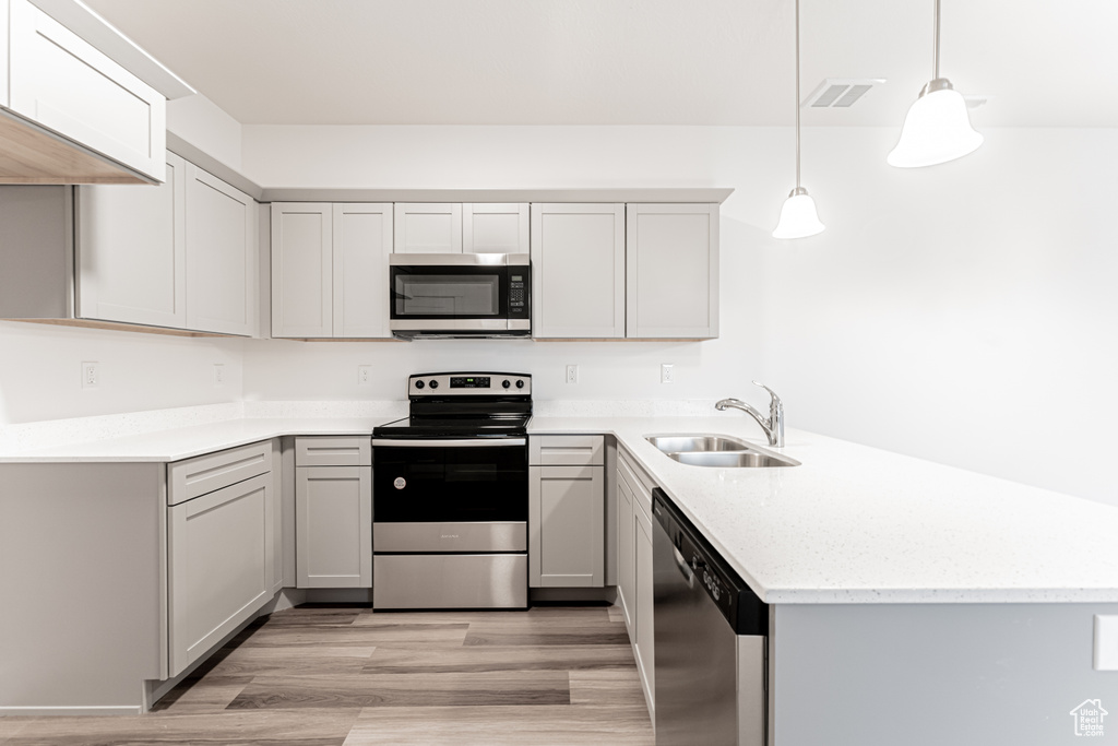 Kitchen featuring visible vents, a peninsula, a sink, stainless steel appliances, and light wood-type flooring