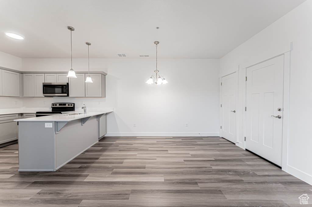 Kitchen featuring a breakfast bar, light wood-style floors, an inviting chandelier, appliances with stainless steel finishes, and a peninsula