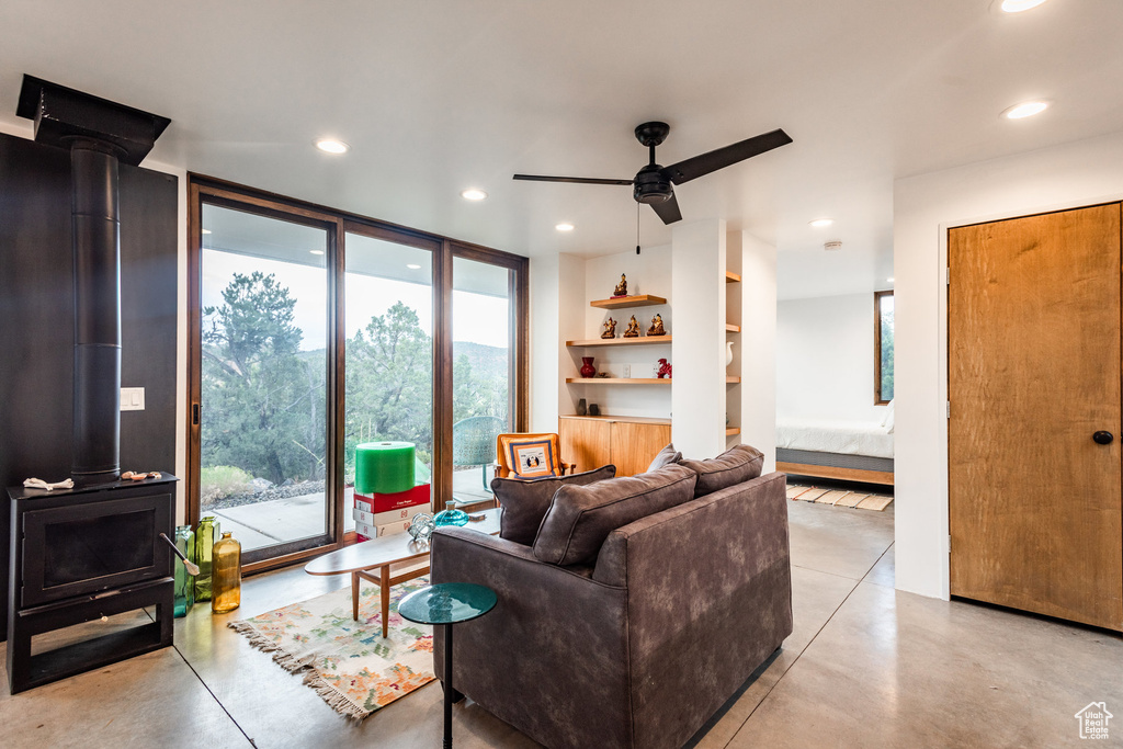 Living room with ceiling fan, a wall of windows, and a wood stove