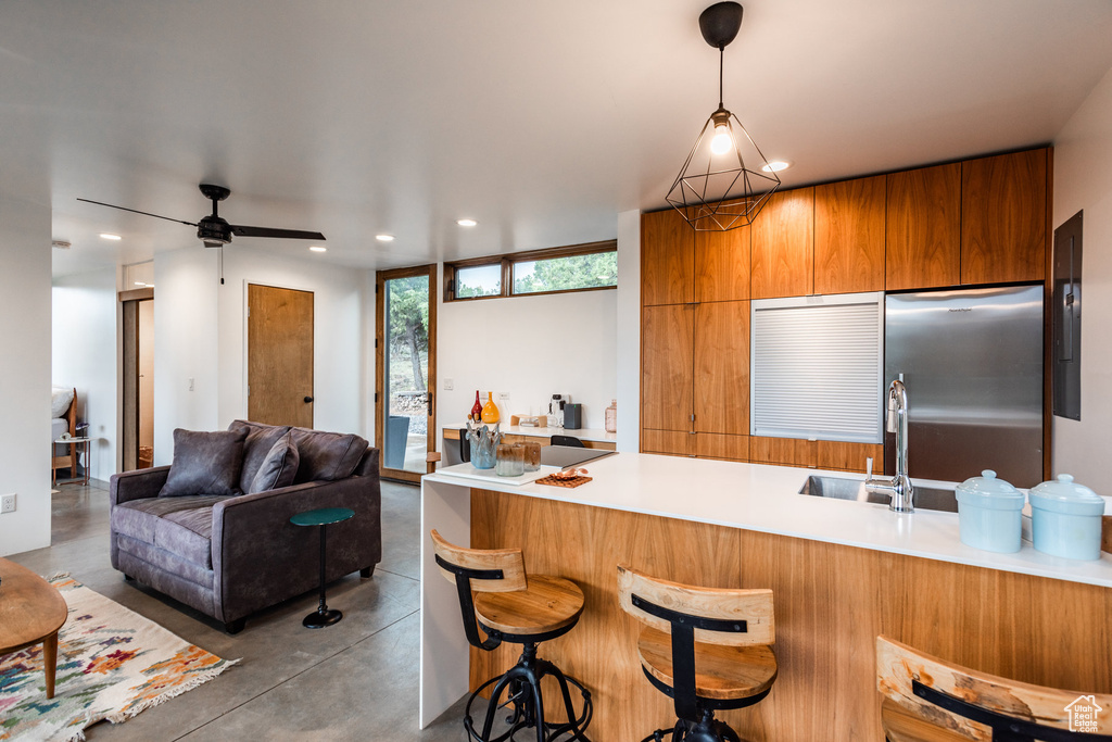 Kitchen featuring a kitchen bar, stainless steel refrigerator, concrete floors, ceiling fan, and hanging light fixtures