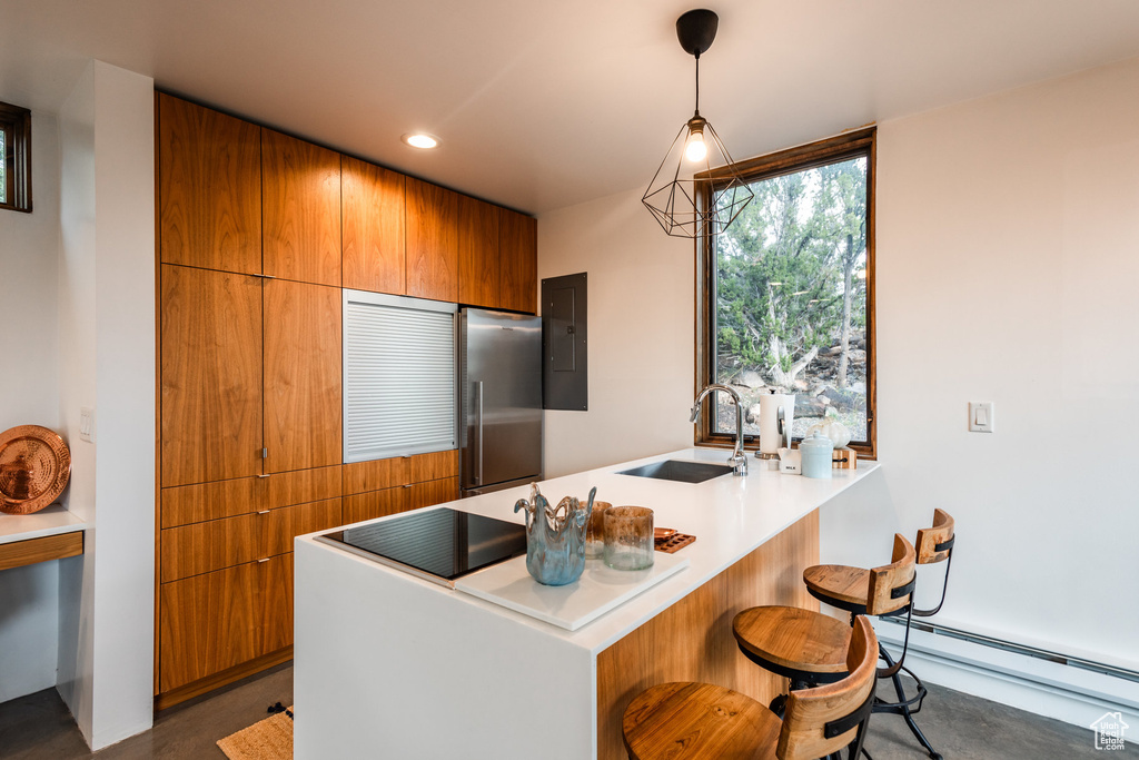 Kitchen with a breakfast bar, sink, decorative light fixtures, baseboard heating, and stainless steel fridge