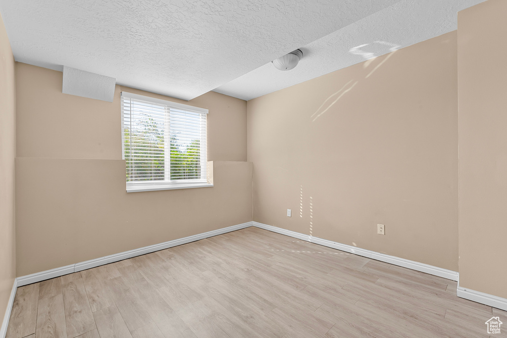 Empty room with a textured ceiling and light hardwood / wood-style floors