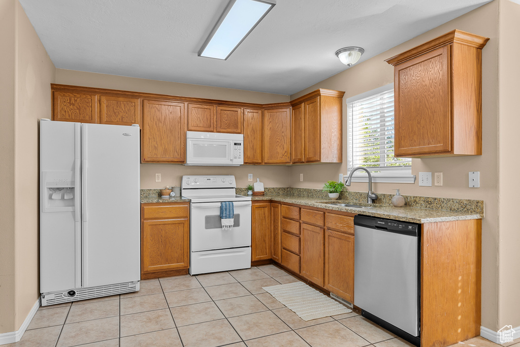 Kitchen featuring sink, light stone countertops, light tile patterned flooring, and white appliances