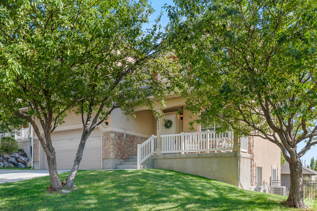 View of property hidden behind natural elements featuring a garage, a porch, and a front yard