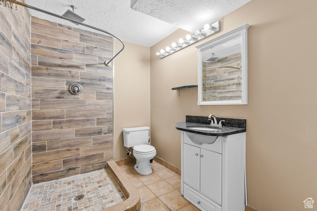 Bathroom with vanity, tile patterned floors, a textured ceiling, tiled shower, and toilet