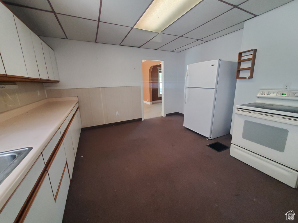 Kitchen with white cabinetry, a drop ceiling, and white appliances