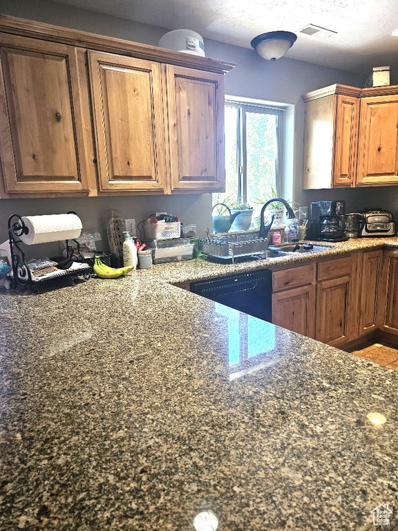 Kitchen featuring sink, a textured ceiling, stone countertops, and dishwasher