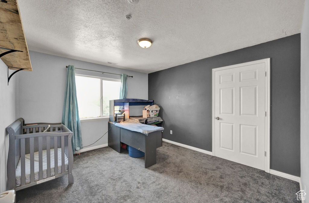 Carpeted bedroom featuring a textured ceiling and a nursery area