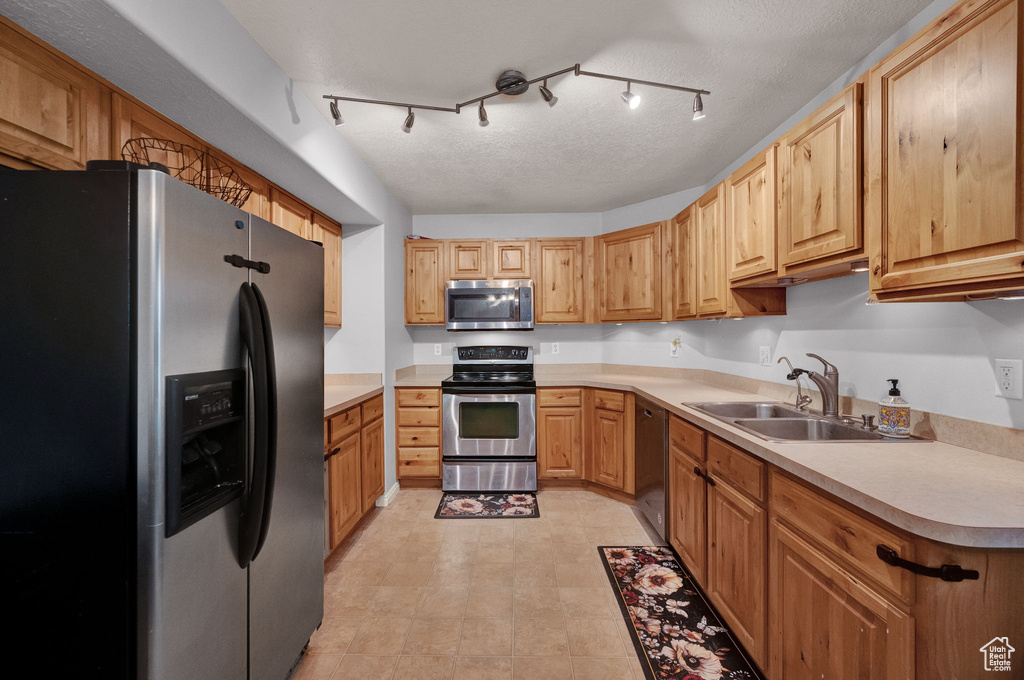 Kitchen featuring light tile patterned floors, appliances with stainless steel finishes, rail lighting, and sink