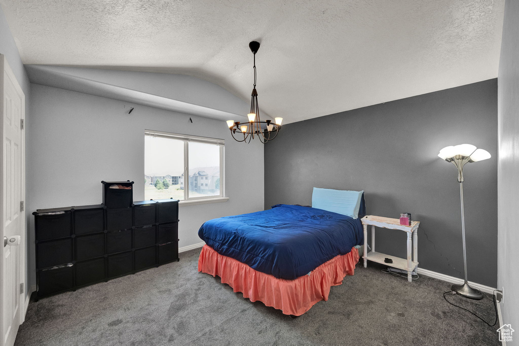 Carpeted bedroom with a textured ceiling, vaulted ceiling, and an inviting chandelier