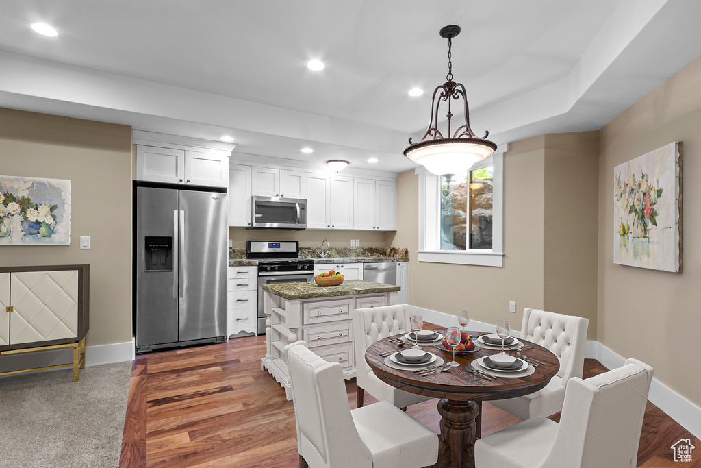 Kitchen featuring carpet, a center island, decorative light fixtures, white cabinetry, and stainless steel appliances