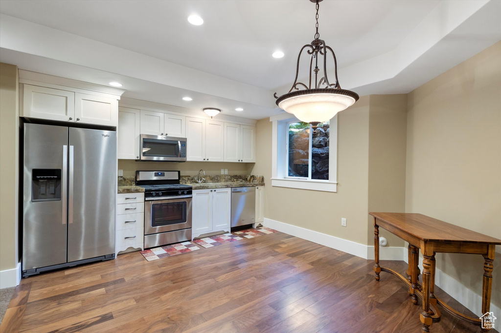 Kitchen with stainless steel appliances, white cabinets, wood-type flooring, dark stone counters, and hanging light fixtures