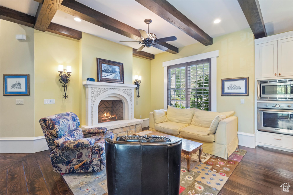 Living room with a fireplace, ceiling fan, dark wood-type flooring, and beamed ceiling