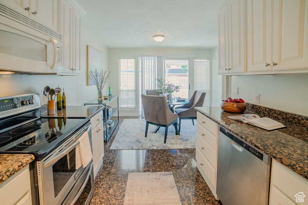 Kitchen featuring dark stone counters, appliances with stainless steel finishes, tile patterned flooring, and white cabinetry