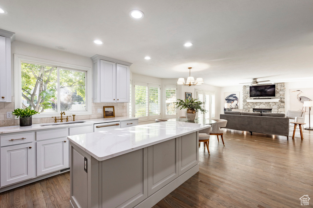 Kitchen featuring white cabinetry, sink, a center island, dark wood-type flooring, and a stone fireplace