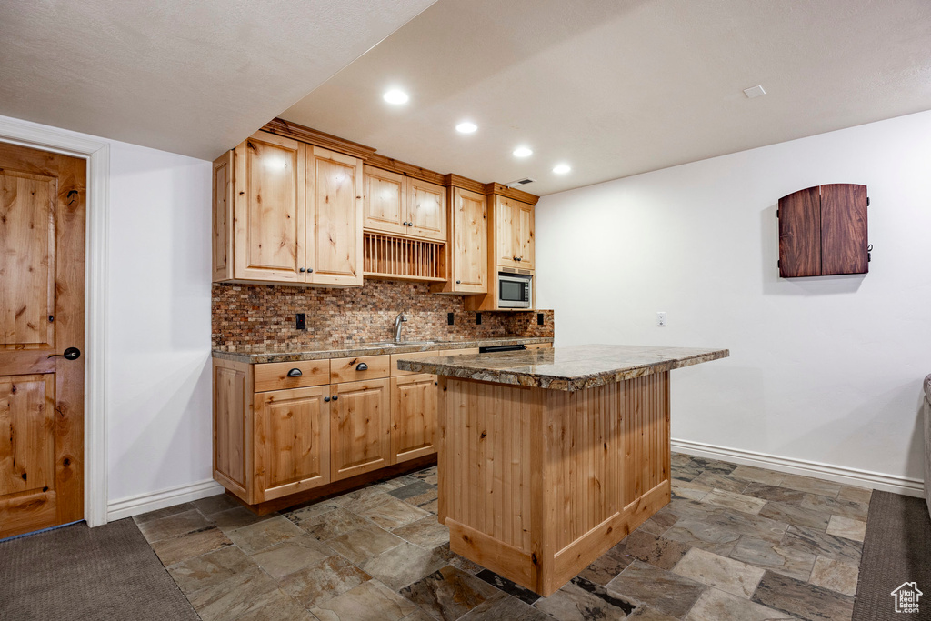 Kitchen featuring tile patterned flooring, light brown cabinetry, tasteful backsplash, and a kitchen island