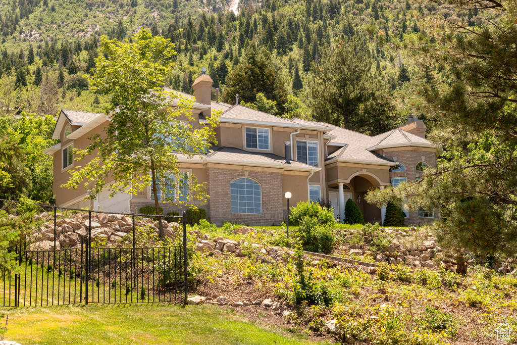 View of front facade featuring a wooded view, stucco siding, a chimney, and brick siding