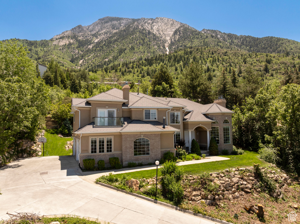 View of front facade with a view of trees, driveway, a chimney, and a mountain view