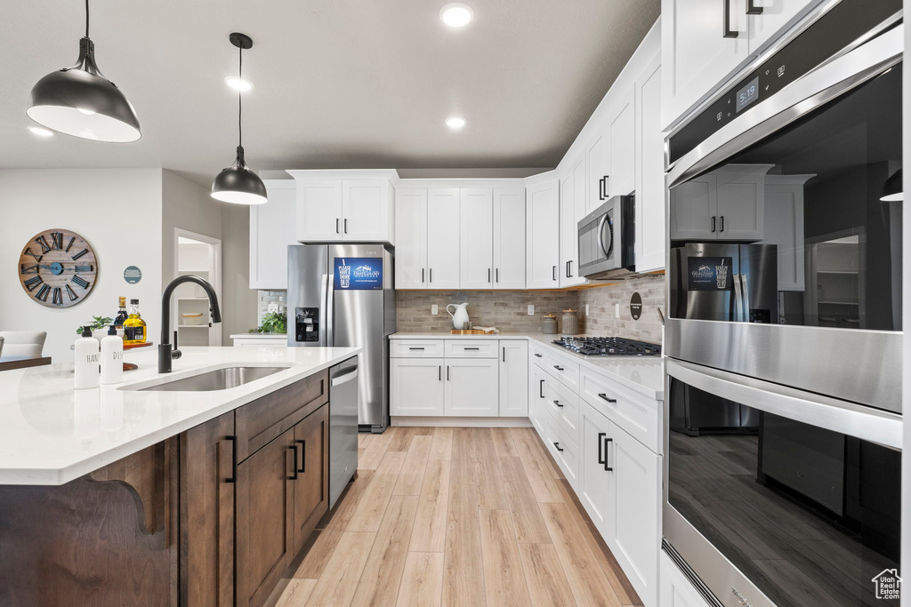 Kitchen featuring appliances with stainless steel finishes, light hardwood / wood-style flooring, decorative backsplash, white cabinetry, and sink