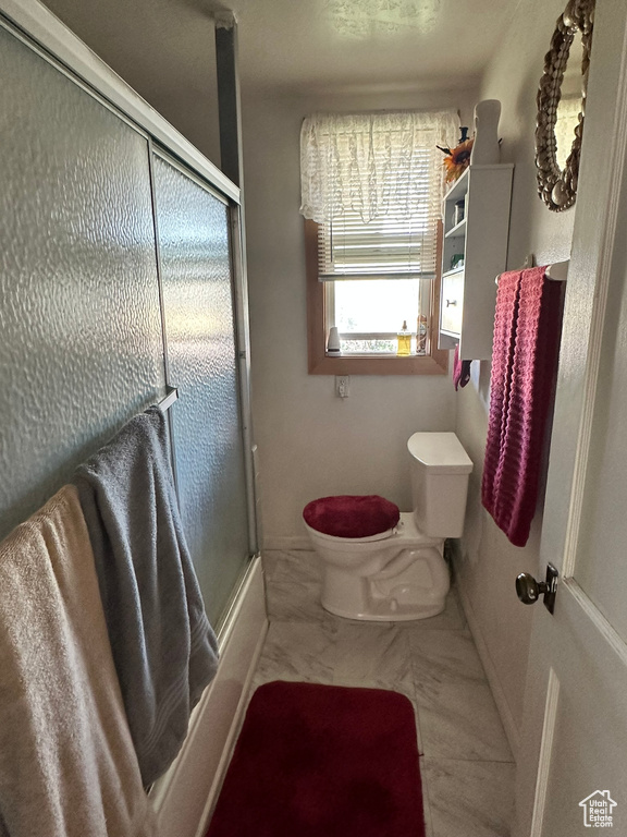 Bathroom featuring enclosed tub / shower combo, tile patterned flooring, and toilet