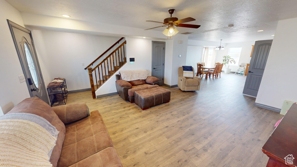 Living room featuring ceiling fan with notable chandelier and light wood-type flooring