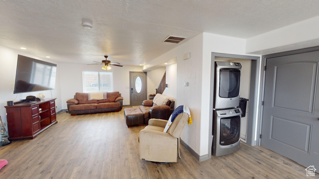 Living room featuring stacked washer / dryer, light wood-type flooring, a textured ceiling, and ceiling fan